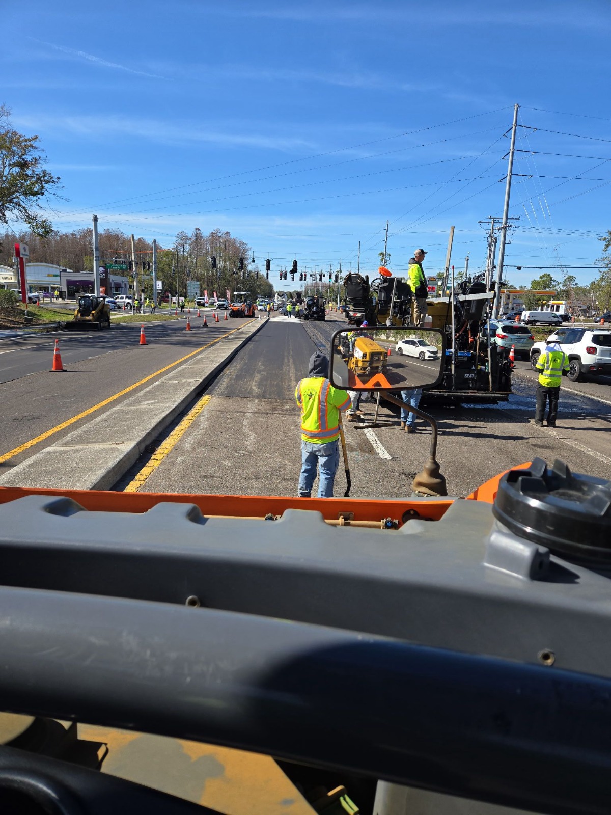 A Florida highway lane under construction in daylight with crew, cones and equipment in the travel way.