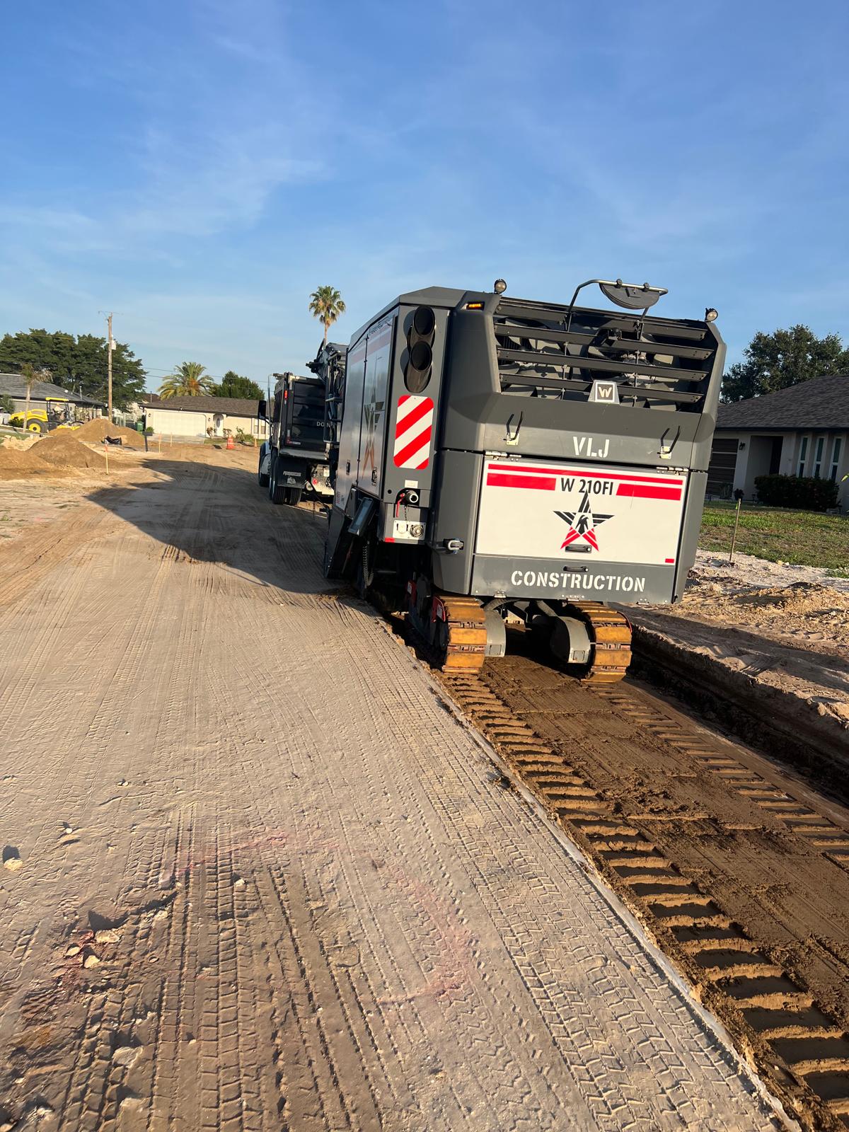 A VLJ Construction Wirtgen W 210Fi milling machine parked on a partially milled residential street.